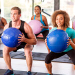 Treino funcional: 2 homens e 3 mulheres fazendo agachamento com bola de peso na academia