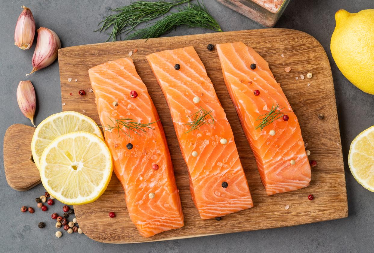 Raw salmon slices with seasonings over wooden board