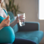 mulher grávida segurando comprimindo e um copo de água