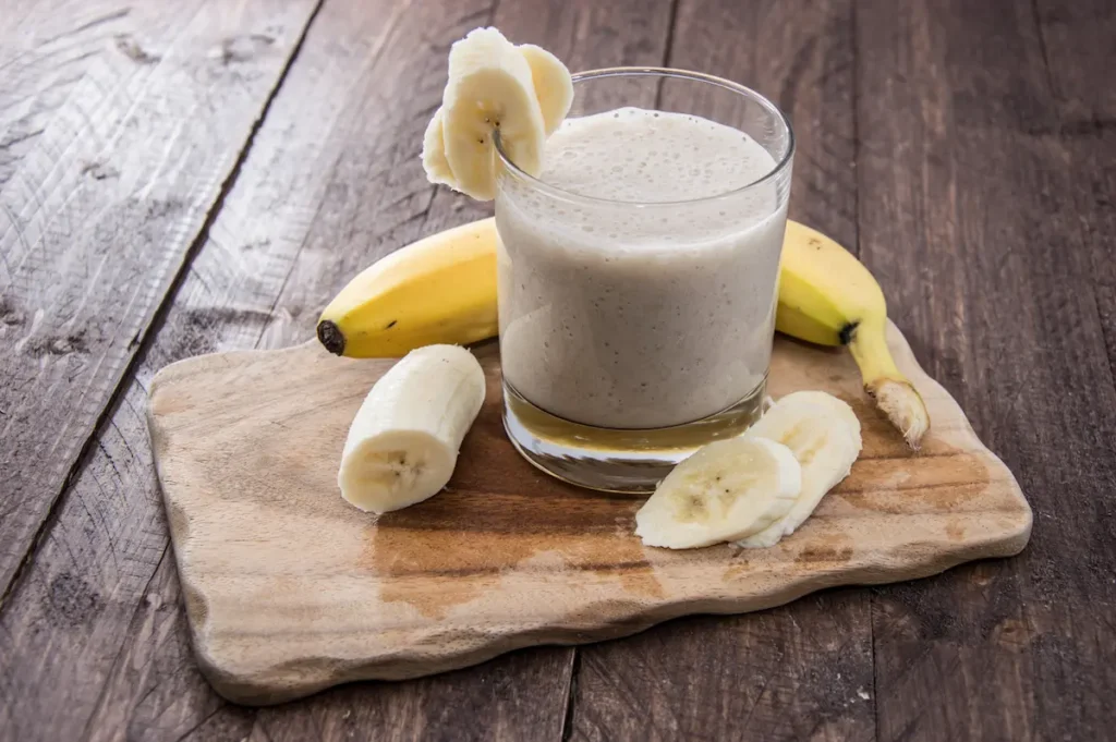 imagem de uma vitamina de banana em uma bandeja de madeira com a fruta ao lado